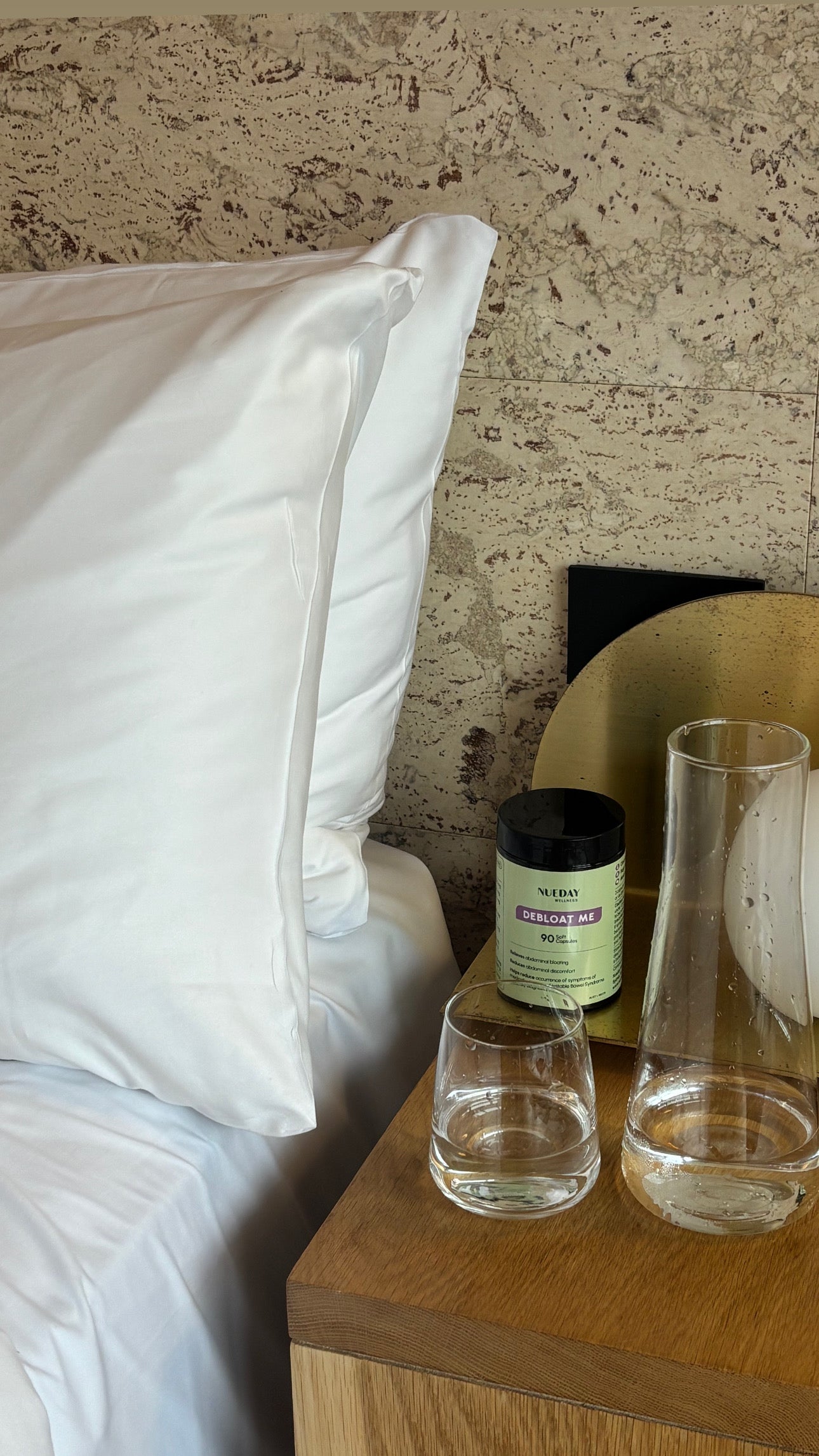 Bedside scene featuring Nueday Wellness Debloat Me capsules and a glass of water.