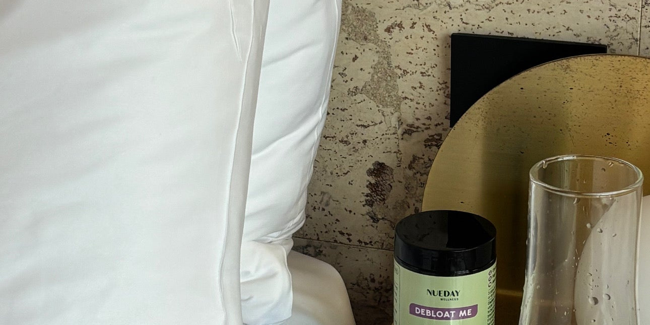 Bedside scene featuring Nueday Wellness Debloat Me capsules and a glass of water.