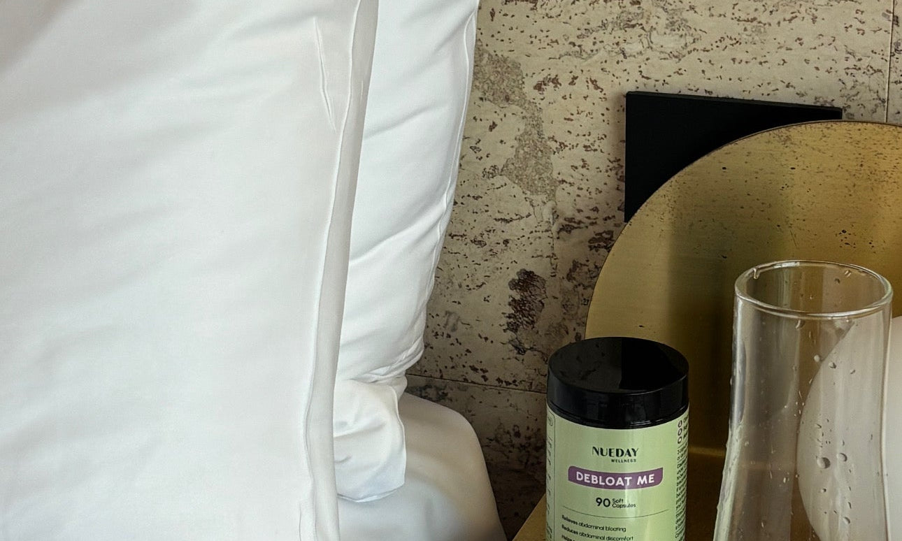 Bedside scene featuring Nueday Wellness Debloat Me capsules and a glass of water.
