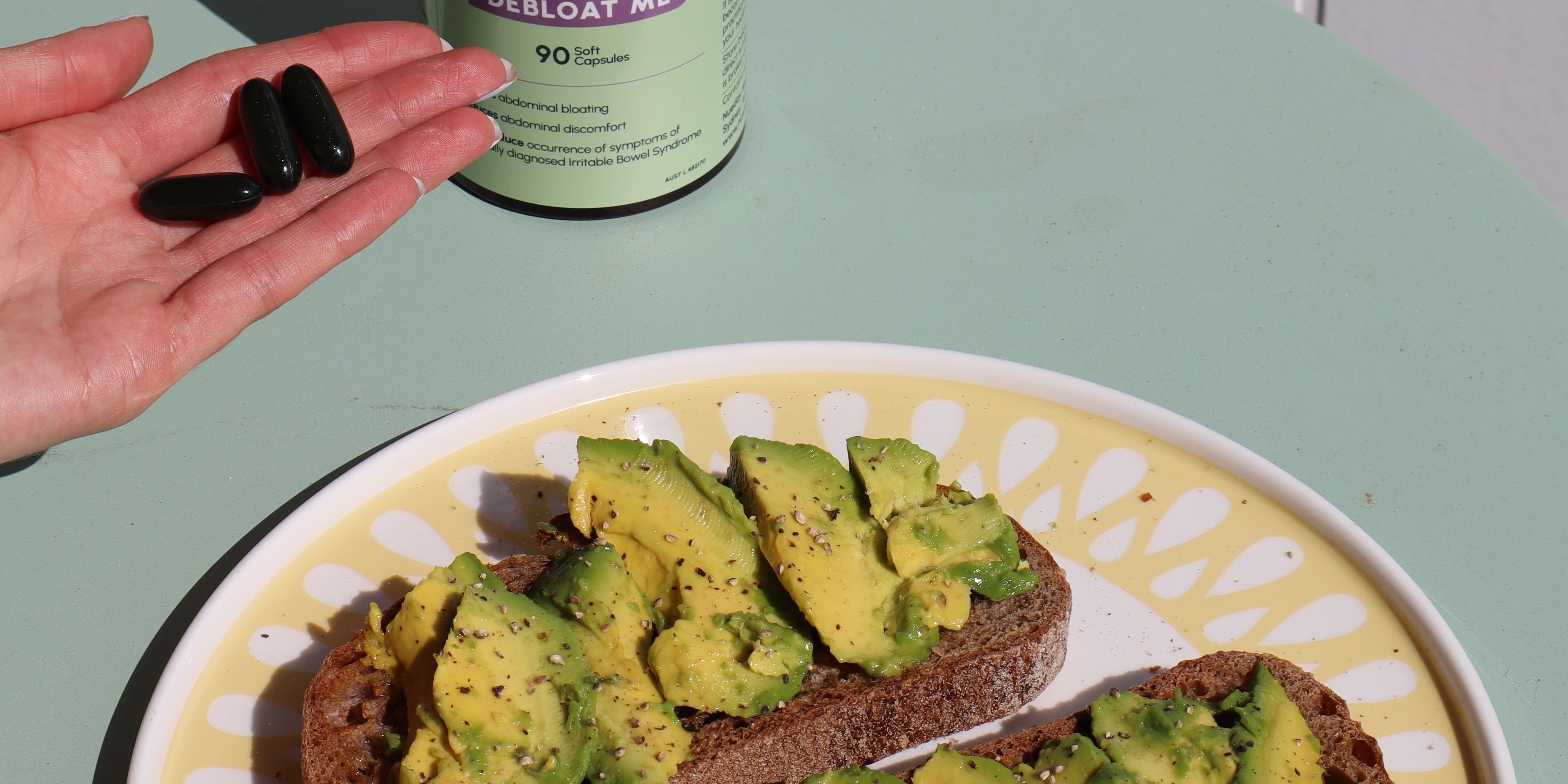 avocado on a plate beside Nueday Wellness Debloat Me supplements, with a woman holding three capsules.
