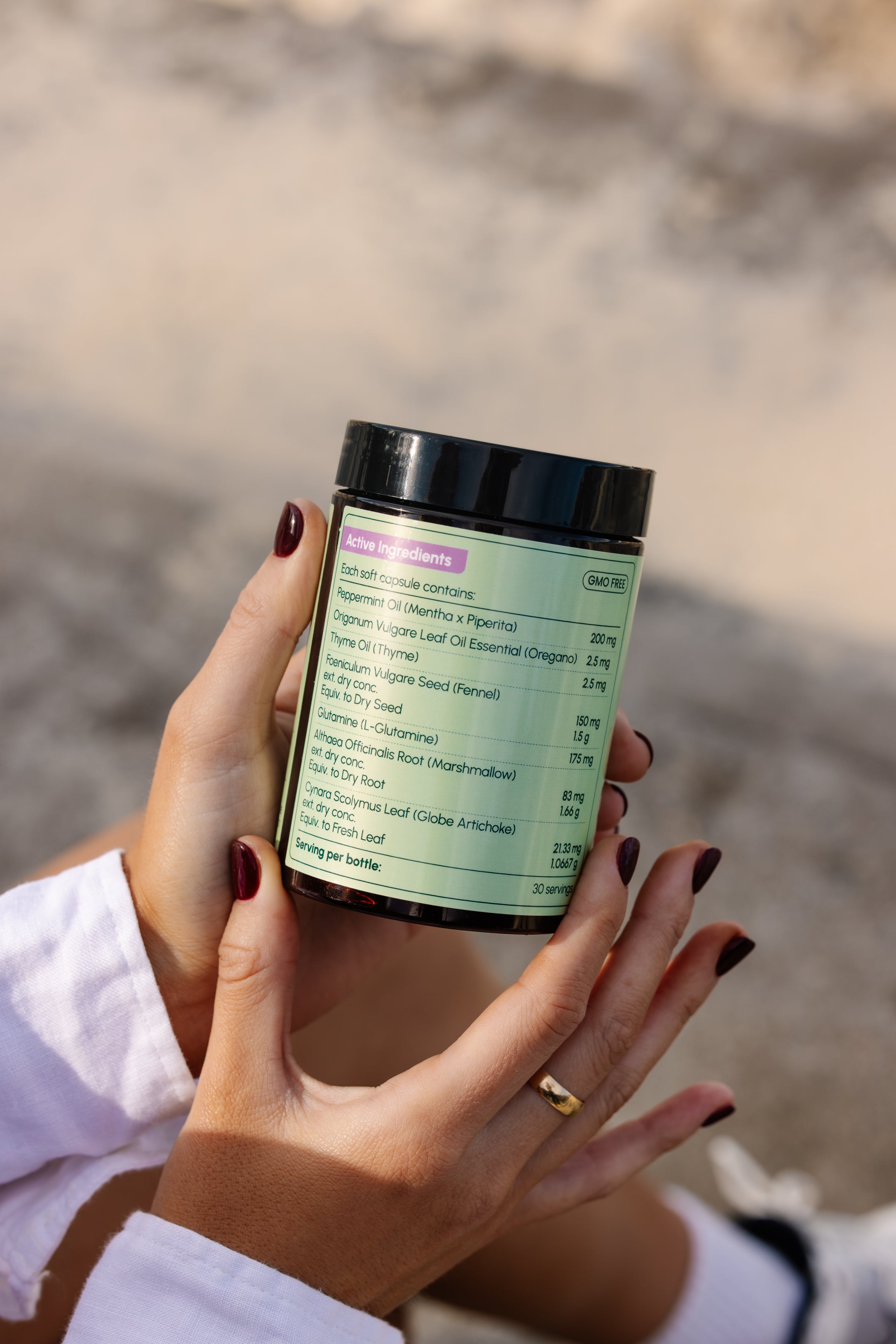 Close-up of a person holding a supplement jar Debloat Me from Nueday Wellness, showing the ingredient label that lists peppermint oil, oregano oil, thyme oil, fennel seed, L-glutamine, marshmallow root, and globe artichoke leaf. 